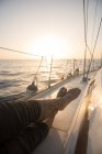 Cultivo piernas de macho acostado en la cubierta lateral de barco caro flotando en el mar ondulante en el día soleado - foto de stock