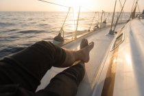 Gambe ritagliate di maschio sdraiato sul ponte laterale di costosa barca galleggiante sul mare ondulato nella giornata di sole — Foto stock
