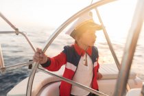 Позитивный ребенок в капитанской шляпе, плавающий на дорогой лодке по морю в солнечный день — стоковое фото