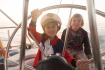 Positive Kinder mit Kapitänsmütze treiben bei sonnigem Wetter auf teurem Boot auf See — Stockfoto