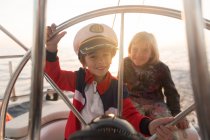 Positive Kinder mit Kapitänsmütze treiben bei sonnigem Wetter auf teurem Boot auf See — Stockfoto