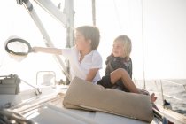 Crianças positivas sentadas no convés lateral do barco caro flutuando na água no dia ensolarado — Fotografia de Stock