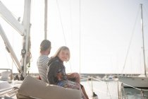 Vista lateral del padre con el niño sentado en la cubierta lateral del barco caro flotando en el agua en el día soleado - foto de stock
