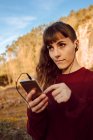 Молода жінка з пірсингом та навушниками слухає музику на мобільному телефоні в сільській місцевості — стокове фото