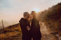 Happy homosexual couple hugging and kissing on path in forest in sunny day — Stock Photo