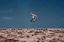 Чоловік стрибає над дахом проти блакитного неба — стокове фото