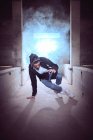 Young man in stylish outfit performing breakdance movement in smoke while dancing inside shabby building — Stock Photo