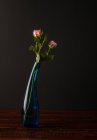 Розовые цветы в стильной стеклянной вазе на деревянном столе на темном фоне — стоковое фото