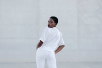 Елегантна модна короткошерста жінка в білому вбранні позує проти сірого будівництва — стокове фото