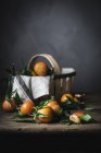 Mandarinas maduras com folhas e cesta em mesa de madeira áspera — Fotografia de Stock