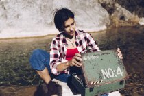 Frau sitzt auf Felsen in transparentem Seewasser und schaut in ein rostiges altes Metallgehäuse beim Picknick — Stockfoto