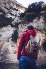 Back view of male with backpack on coast of mountain river near rock mountain — Stock Photo