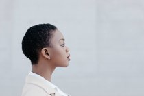 Primo piano della donna etnica dai capelli corti in posa contro il muro grigio — Foto stock