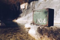 Caixa de metal velho colocado em rocha áspera em água transparente do lago à luz do sol — Fotografia de Stock