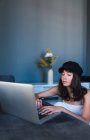 Mulher elegante jovem atraente em cap usando laptop em casa — Fotografia de Stock