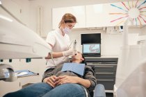 Женщина в перчатках и маске с использованием современного оборудования для сканирования зубов пациентки в стоматологическом кабинете — стоковое фото