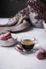 Taza de café espresso con macarrones en la mesa con flores - foto de stock