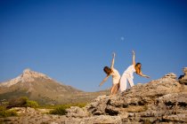 Giovani donne misteriose con le mani alzate in posa su rocce vicino collina e cielo blu con la luna — Foto stock