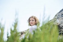 Young charming woman sitting between rock and branches and looking at camera — Stock Photo