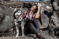 Joyeuse jeune femme assise près husky sur le rocher — Photo de stock