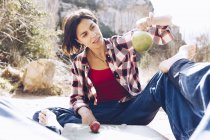Man lying on plaid with woman sitting near and tossing apple up enjoying time together on picnic in nature — Stock Photo