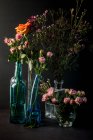 Glass vases with bouquets of lovely flowers on black background — Stock Photo