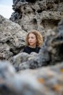 Jovem mulher pensativa sentada em rochas e olhando para longe — Fotografia de Stock