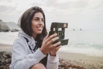 Smiling young woman holding camera on beach — Stock Photo