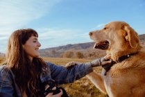 Vue latérale de la jeune femme tirant sur la caméra chien drôle entre prairie et ciel bleu — Photo de stock