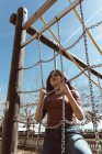 Jovem mulher sonhadora apoiada em correntes e olhando para longe no parque infantil da cidade — Fotografia de Stock