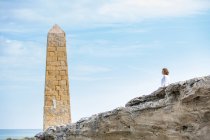 Жінка стоїть біля кам'яного будівництва у вигляді вежі на скелястому узбережжі моря — стокове фото