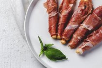Gressinis with spanish typical serrano ham on white platter — Stock Photo