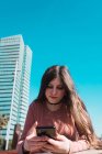 Adolescente regardant son smartphone dans la rue par une journée ensoleillée — Photo de stock
