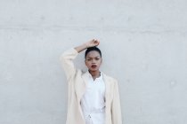 Elegante donna etnica dai capelli corti alla moda in abito bianco in posa contro muro grigio — Foto stock