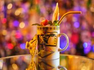 Ornamental mug of tasty cocktail decorated with exotic fruits and straw on table in bar — Stock Photo