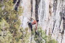 Vista laterale di un maschio irriconoscibile in pantaloncini che si arrampica su una ruvida scogliera nella giornata di sole in campagna — Foto stock