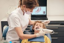 Frau in Maske und Arztuniform macht Scan der Zähne eines kleinen Jungen während der Arbeit in der Zahnarztpraxis — Stockfoto
