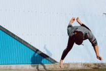 Ragazzo scalzo in abito elegante esecuzione flip vicino al muro di edificio moderno sulla strada della città — Foto stock