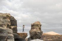 Side view of unrecognizable woman taking photos of beautiful countryside while standing amidst rough stone pillars against overcast sky — Stock Photo