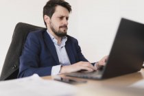 Konzentrierter junger Mann surft am Laptop am Tisch im Büro — Stockfoto