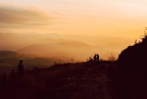 Couple homosexuel lointain embrassant près du chien sur la route dans les montagnes au coucher du soleil — Photo de stock