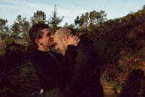Feliz pareja homosexual abrazándose en el camino en el bosque en el día soleado - foto de stock