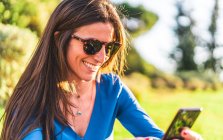 Ritratto di giovane donna con occhiali da sole utilizzando smartphone seduta — Foto stock
