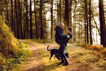 Homosexual couple embracing near dog on route in forest in sunny day — Stock Photo
