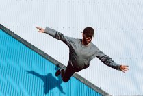 Kerl in stylischem Outfit beim Flip in der Nähe der Mauer eines modernen Gebäudes an der Stadtstraße — Stockfoto