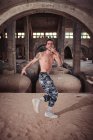 Shirtless man dancing on sand in old shabby building — Stock Photo