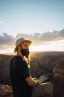 Вид сбоку на бородатого парня с рюкзаком, смотрящего на красивый каньон и спокойную реку в солнечный день на западном побережье США — стоковое фото