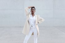 Мода короткошерста етнічна жінка в білому вбранні позує на сіру стіну — стокове фото