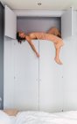 Giovane donna sensuale dormire su alto ripiano di armadio vicino a letto in camera da letto — Foto stock