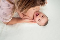 Dall'alto madre che gioca con divertente piccolo neonato nudo sdraiato sul letto in camera — Foto stock